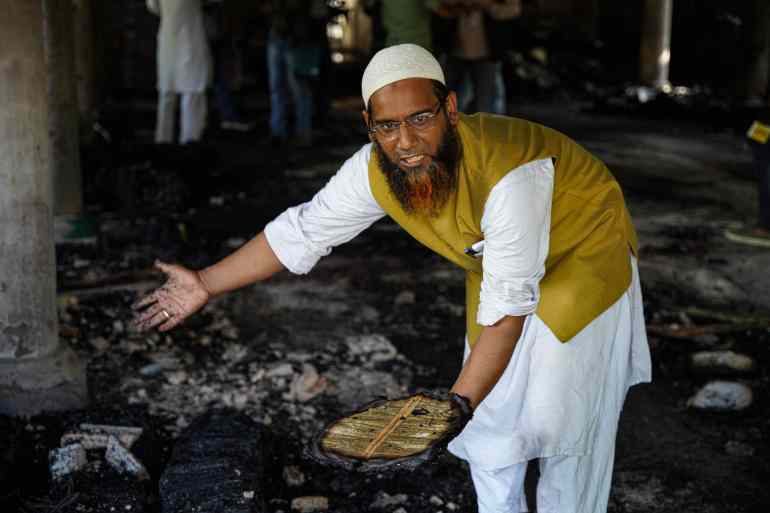 Mohammad Shahabuddin pointing to pile ash books as he holds a half burnt Quran in his hand at Azizia Madrasa in Nalanda Bihar.