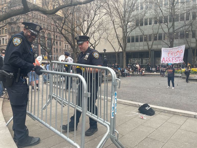 Two police officers converse over two barricades, while a protester holds a sign in an increasingly empty street