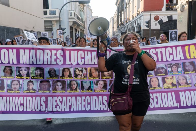 Magali Aguilar speaks into a bullhorn as women carry a banner featuring the faces of women who have faced gender-based violence