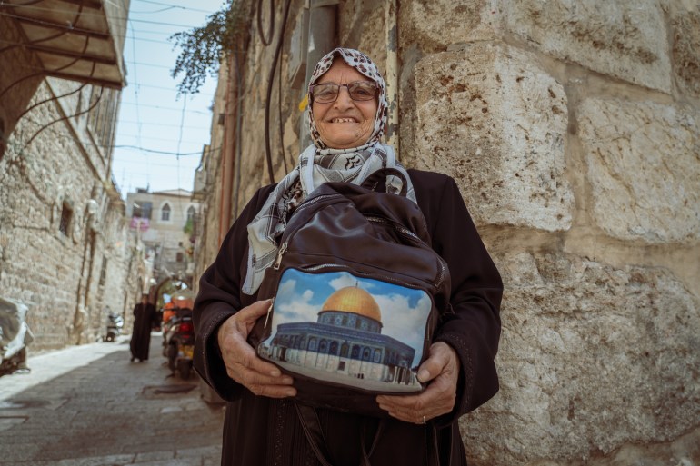 Elderly woman displays a tote bag bearing the image of the Dome of the Rock