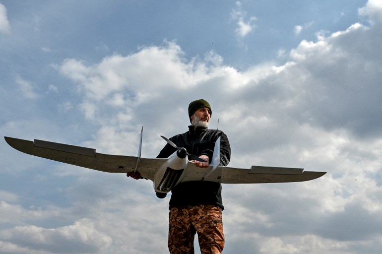 A photo of a serviceman holding a drone that looks like an airplane.