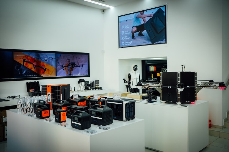 A photo of two tables filled with drone gear and one long television screen on the left wall and a regular size television screen on the top right wall.