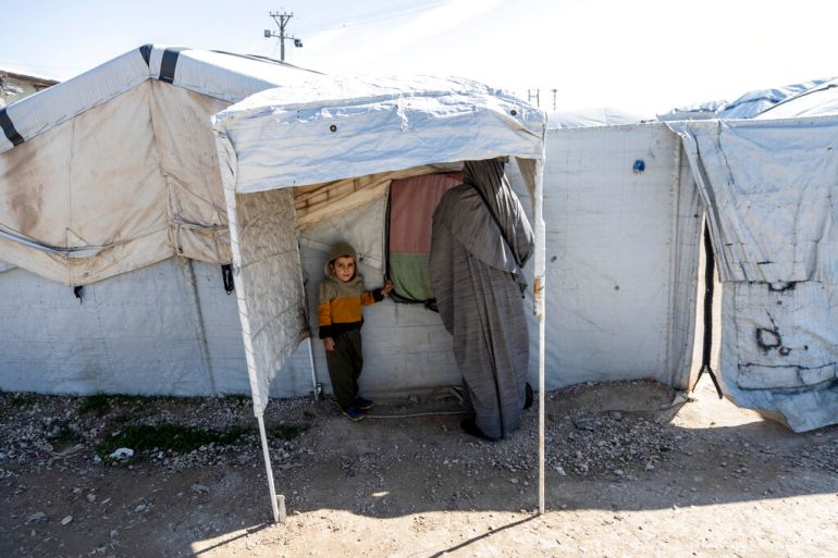A woman and a child stand under a tent in a Syrian detention camp