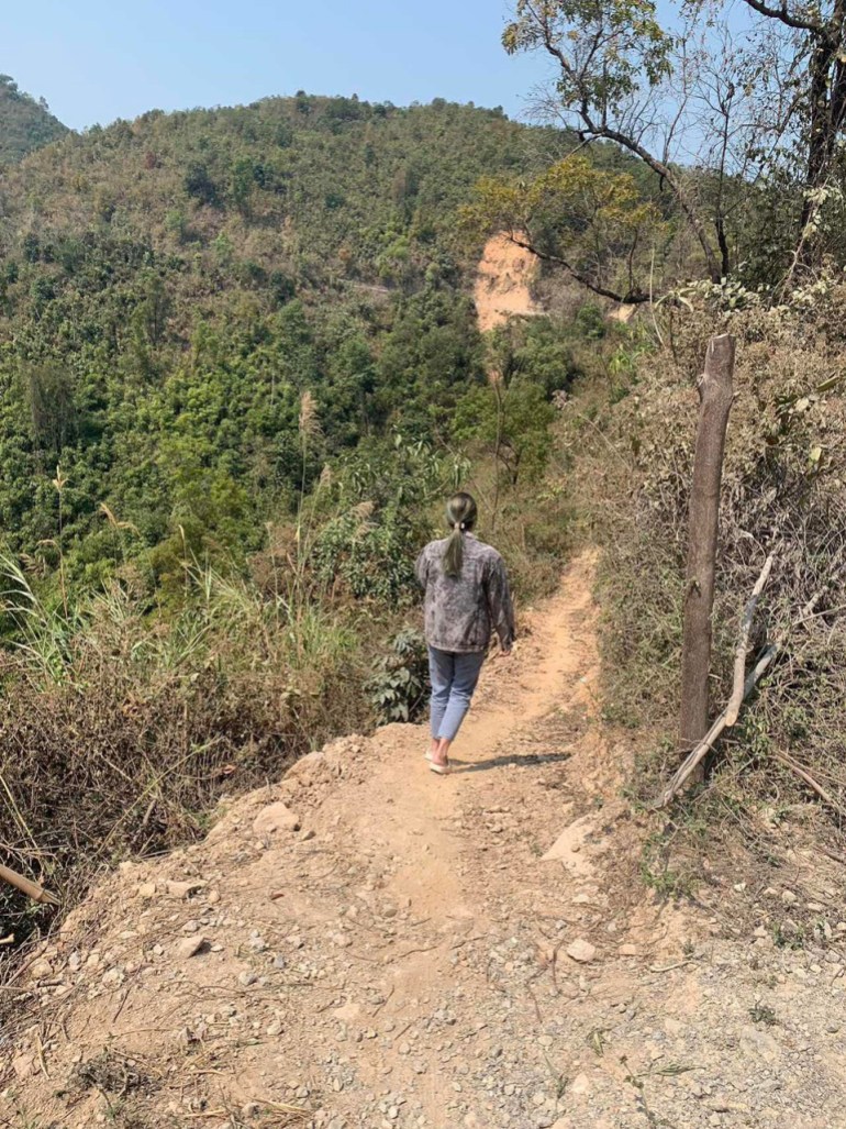 A woman walking along a rocky path in a hilly landscape. She is walking away from the camera.