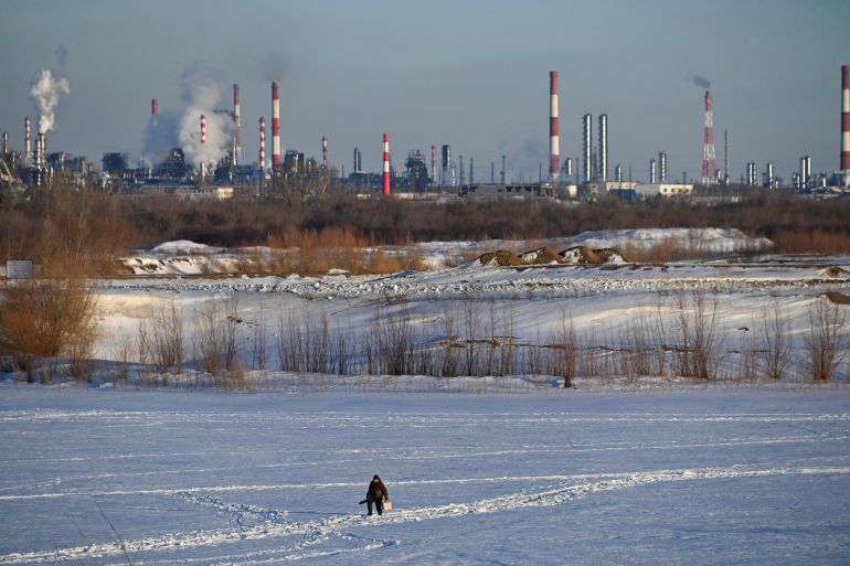 A fisherman walks on the ice-covered Irtysh River near an oil refinery and a thermal power station in the Siberian city of Omsk