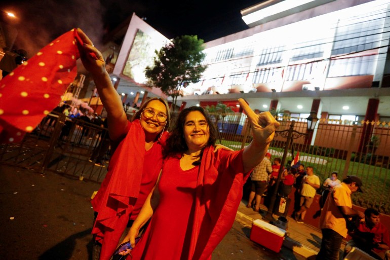Two women celebrate Pena's victory on the streets of Asuncion. They are wearing red, smiling and have their hands in the air.