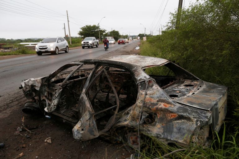 A burned car sits empty on the side of a road