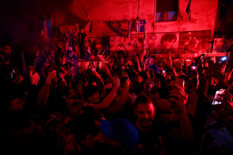Fans Napoli merayakan kemenangan Serie A.  Foto-foto besar Diego Maradona dapat dilihat di dinding gedung terdekat.