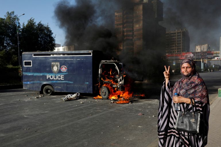Uma mulher gesticula ao lado de um veículo policial em chamas durante um protesto dos apoiadores do ex-primeiro-ministro do Paquistão, Imran Khan, após sua prisão, em Karachi