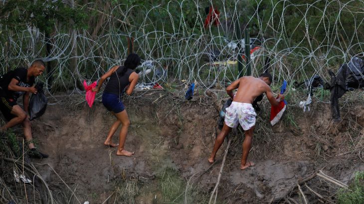 Migrants and refugees try to climb a fence on the US-Mexico border