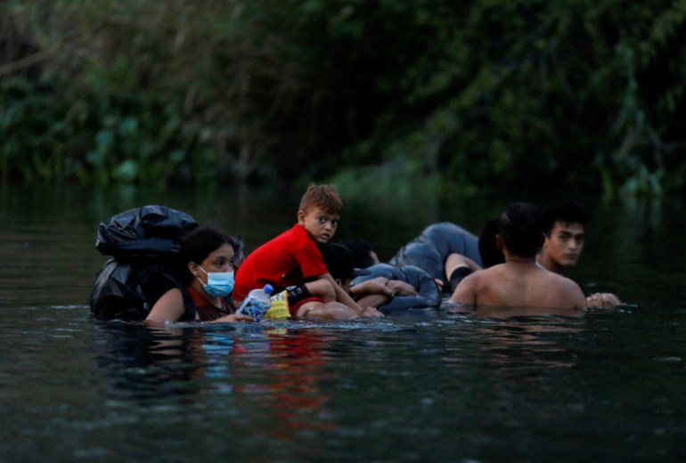 Asylum seekers wade through the water of the Rio Bravo River to cross the US-Mexico boder