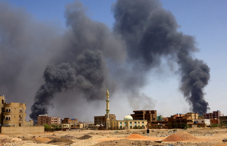 Seorang pria berjalan saat asap mengepul di atas bangunan setelah pengeboman udara, selama bentrokan antara Pasukan Pendukung Cepat paramiliter dan tentara di Khartoum Utara