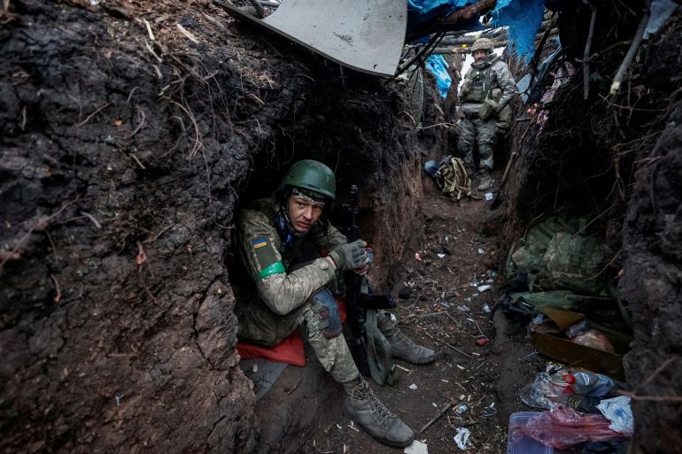 A Ukrainian soldier takes a rest in a trench near the front line in Bakhmut, Ukraine. Other soldiers are behind him in the trench.