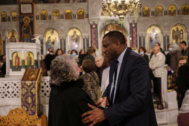 Conservative New Democracy party candidate Spiros Richard Hagabimana greets a woman during mass at the Agia Triada church at the neighbourhood of Nikaia near Athens