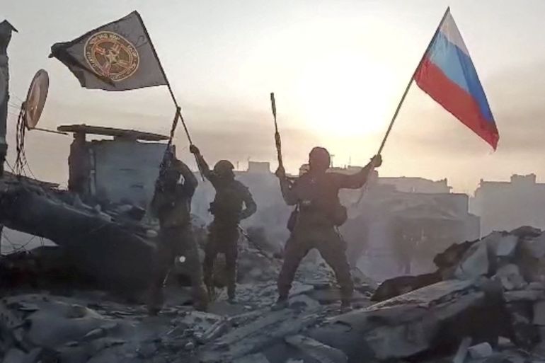 Mercenary fighters wave flags of Russia and the Wagner group on top of a building in an unidentified location.