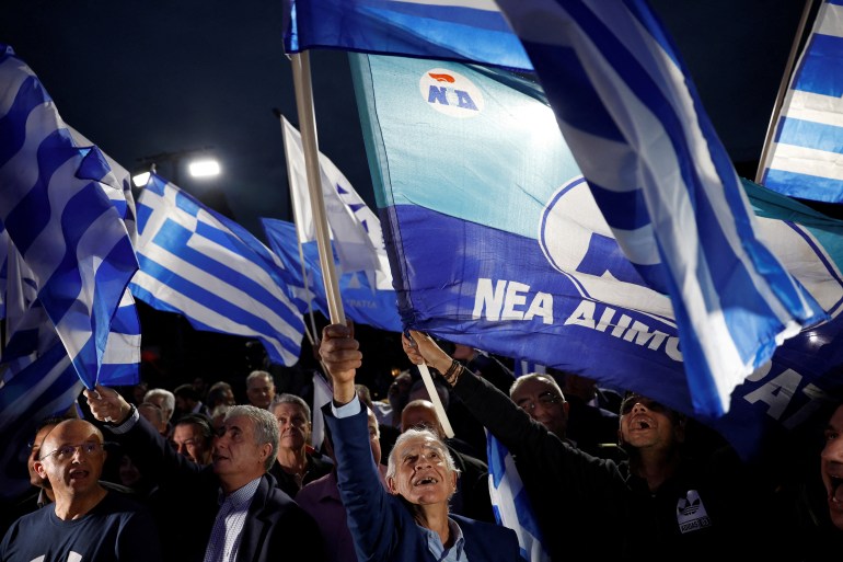 Apoiadores do partido Nova Democracia agitam a bandeira grega listrada de azul e branco e faixas do partido enquanto comemoram sua vitória.