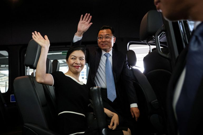 Xie Feng, China's new ambassador to the US, waves as he gets into a waiting car after arriving in the US. His wife is with him and she is waving too. They are both smiling.
