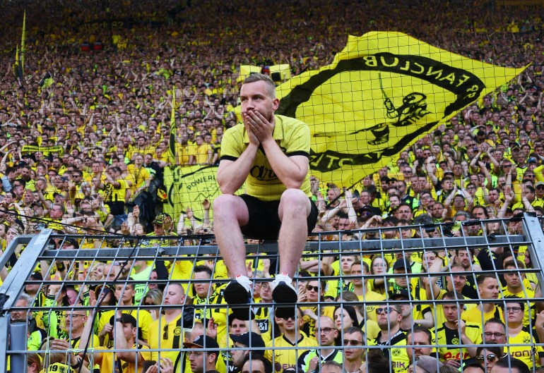 A Dortmund fan sits on the top of the pitch's perimeter fence looking dejected