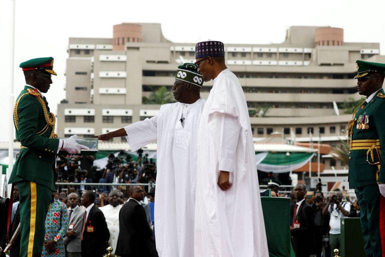 Nigeria's President Bola Tinubu stands next to his predecessor Muhammadu Buhari, as he receives the new flags folded in a glass box, during his swearing-in ceremony in Abuja, Nigeria May 29, 2023. [Temilade Adelaja/Reuters]