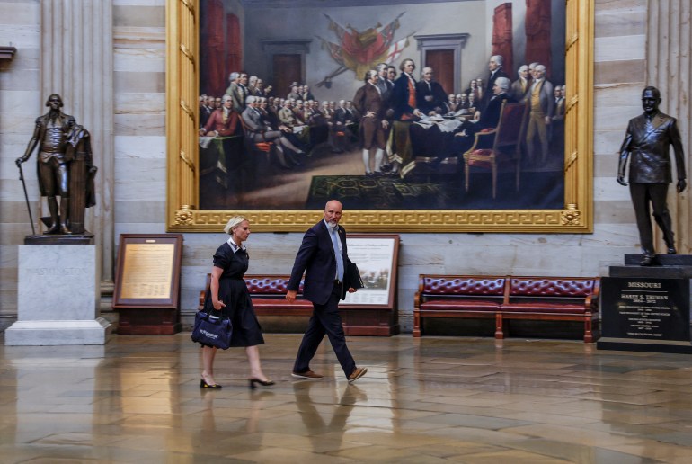 مردی با کت و شلوار و کراوات در طبقات کنگره راه می رود و از کنار تابلوی نقاشی غول پیکر پدران بنیانگذار ایالات متحده می گذرد.  زنی به دنبال او می آید، احتمالاً ویکتوریا اسپارتز، که لباس مشکی با کیف به تن دارد.