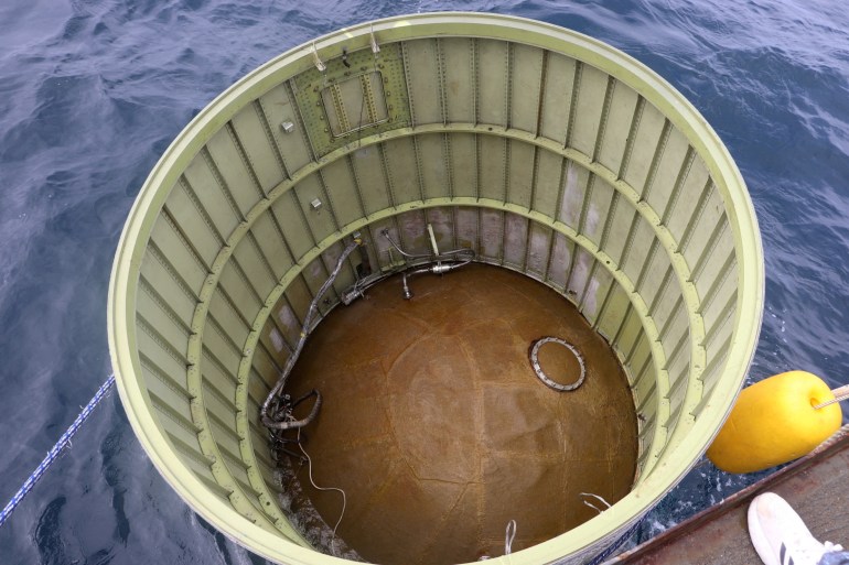 A close up of a barrel shaped object pulled from the sea. There is a brown device inside at the bottom.