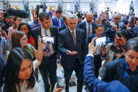 US House Speaker Kevin McCarthy walks across the tiled floors of Congress, surrounded by reporters and people recording on cellphones