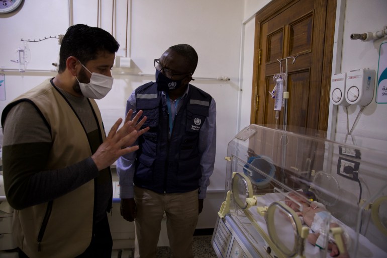 Dua pria berdiri di samping bayi di inkubator