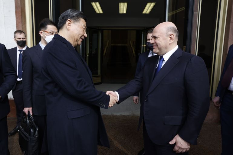 Russian Prime Minister Mikhail Mishustin smiling as he meets China's President Xi Jinping in Moscow. The two men are shaking hands.