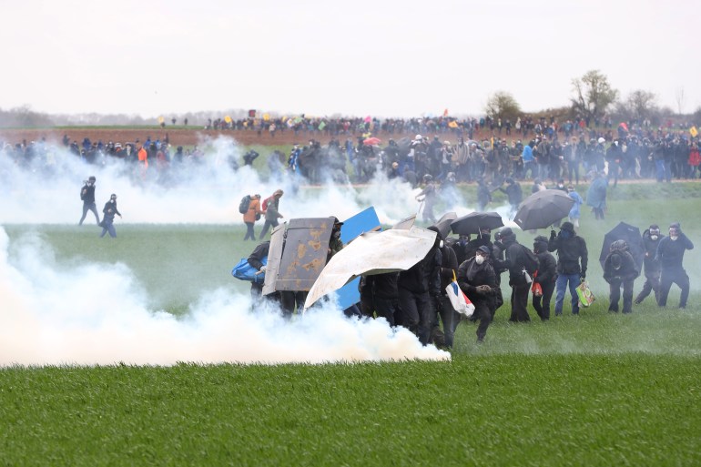 Protesters, surrounded by tear gas, clash with riot mobile gendarmes during a demonstration called by the collective "Bassines non merci", the environmental movement "Les Soulevements de la Terre" and the French trade union 'Confederation paysanne' to protest against the construction of a new water reserve for agricultural irrigation, in Sainte-Soline, central-western France, on March 25, 2023. - More than 3,000 police officers and gendarmes have been mobilised and 1,500 "activists" are expected to take part in the demonstration, around Sainte-Soline. The new protest against the "bassines", a symbol of tensions over access to water, is taking place under thight surveillance on March 25, 2023 in the Deux-Sevres department. (Photo by Yohan Bonnet / AFP)