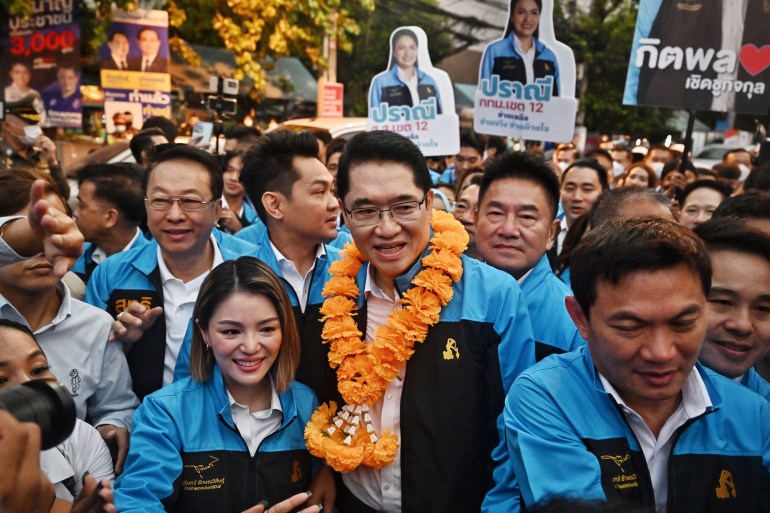 Jurin Laksanawisit, pimpinan Partai Demokrat dikelilingi pendukung.  Dia memiliki karangan bunga marigold emas di lehernya. 