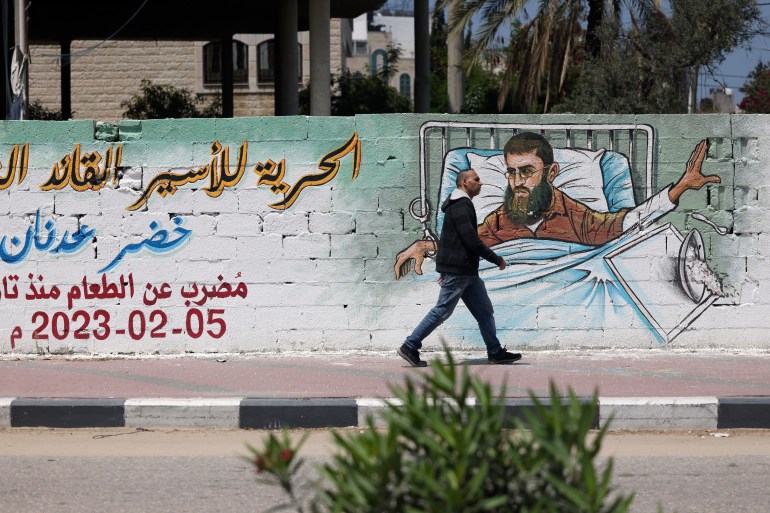 Seorang pria Palestina berjalan melewati grafiti Khader Adnan, seorang warga Palestina yang melakukan mogok makan yang dipenjara di penjara Israel, di Kota Gaza pada 17 April 2023. (Foto oleh Mohammed ABED/AFP)