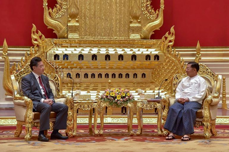 Qin Gang and Min Aung Hlaing. They are sitting on golden chairs in front of a golden sculpture. The walls are red.