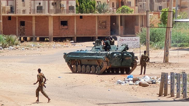 Sudanese Army sodliers walk near armoured vehicles stationed on a street in southern Khartoum