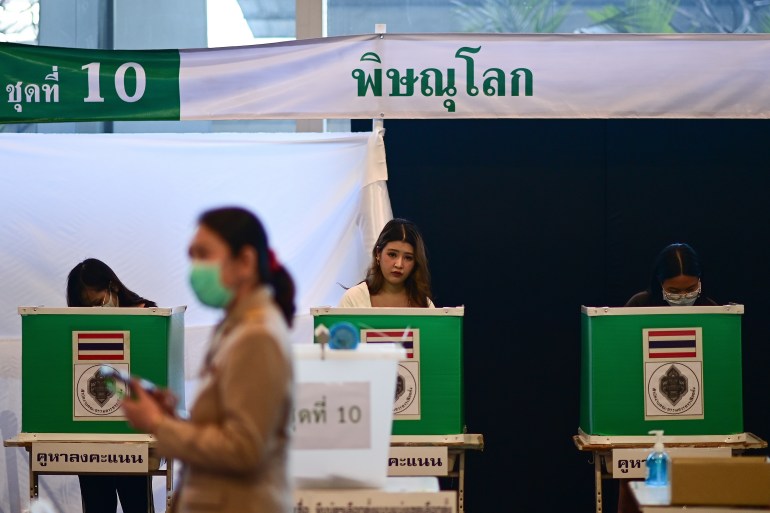 Early voting in the Thai election on May 7. There is a row of green voting booths with two of them occupied. A woman is walking in front.