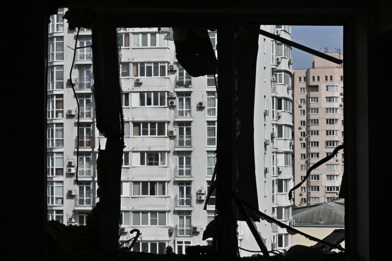 The view from the window of a heavily damaged flat in Kyiv. The window is silhouetted. There are other buildings behind.