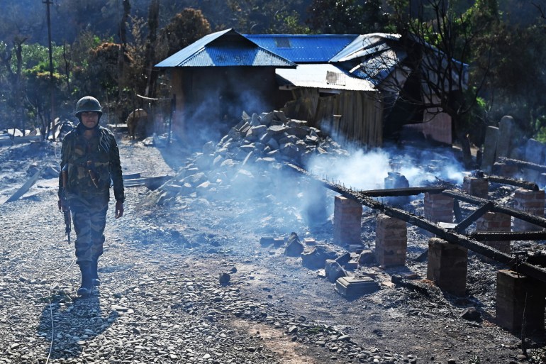 An Indian army soldier walks past the remains of a house that was set on fire by a mob in the ethnic violence hit area of Heiroklian village in Senapati district, in India's Manipur