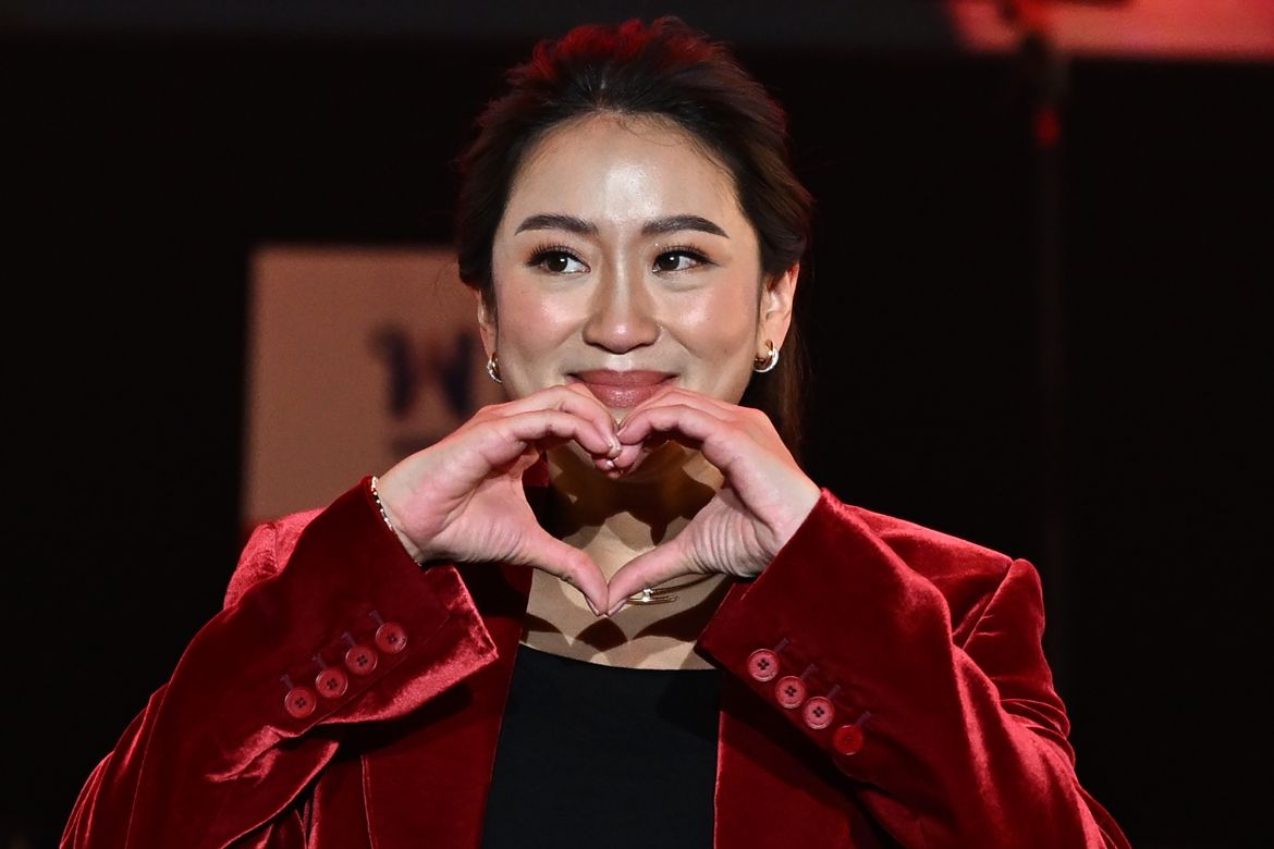 Paetongtarn Shinawatra makes a heart shape with her hands as she looks at her supporters. She is wearing a red jacket and smiling.