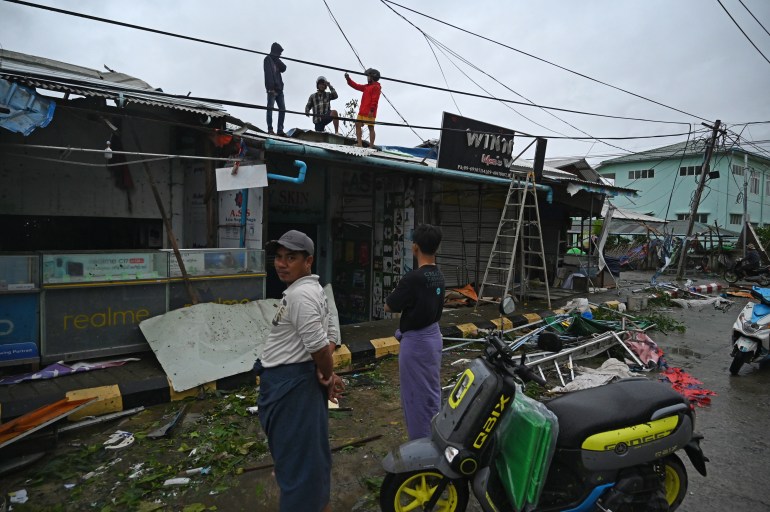 People standing on the roof as others on the ground look at the damage from Cyclone Mocha