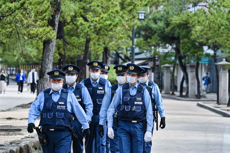 الشرطة اليابانية في دورية بالقرب من هيروشيما ، اليابان ، قبل قمة مجموعة السبع.  إنهم يسيرون على طول مسار تصطف على جانبيه الأشجار.