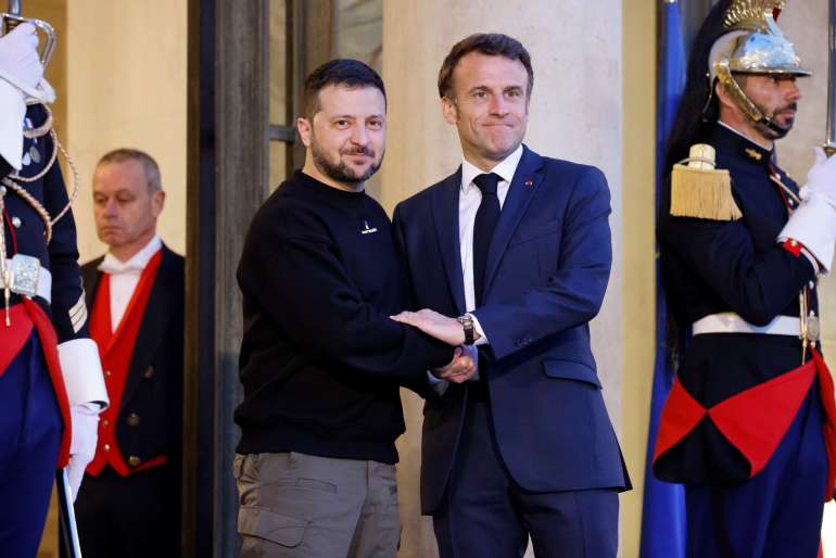 에마뉘엘 마크롱 프랑스 대통령이 프랑스 파리 엘리제궁에서 볼로디미르 젤렌스키 우크라이나 대통령을 영접하고 있다.  Macron은 파란색 정장과 넥타이를, Zelenksyy는 검은색 스웨트 셔츠와 카키색 바지를 입고 있습니다.  그들은 단호해 보입니다. 