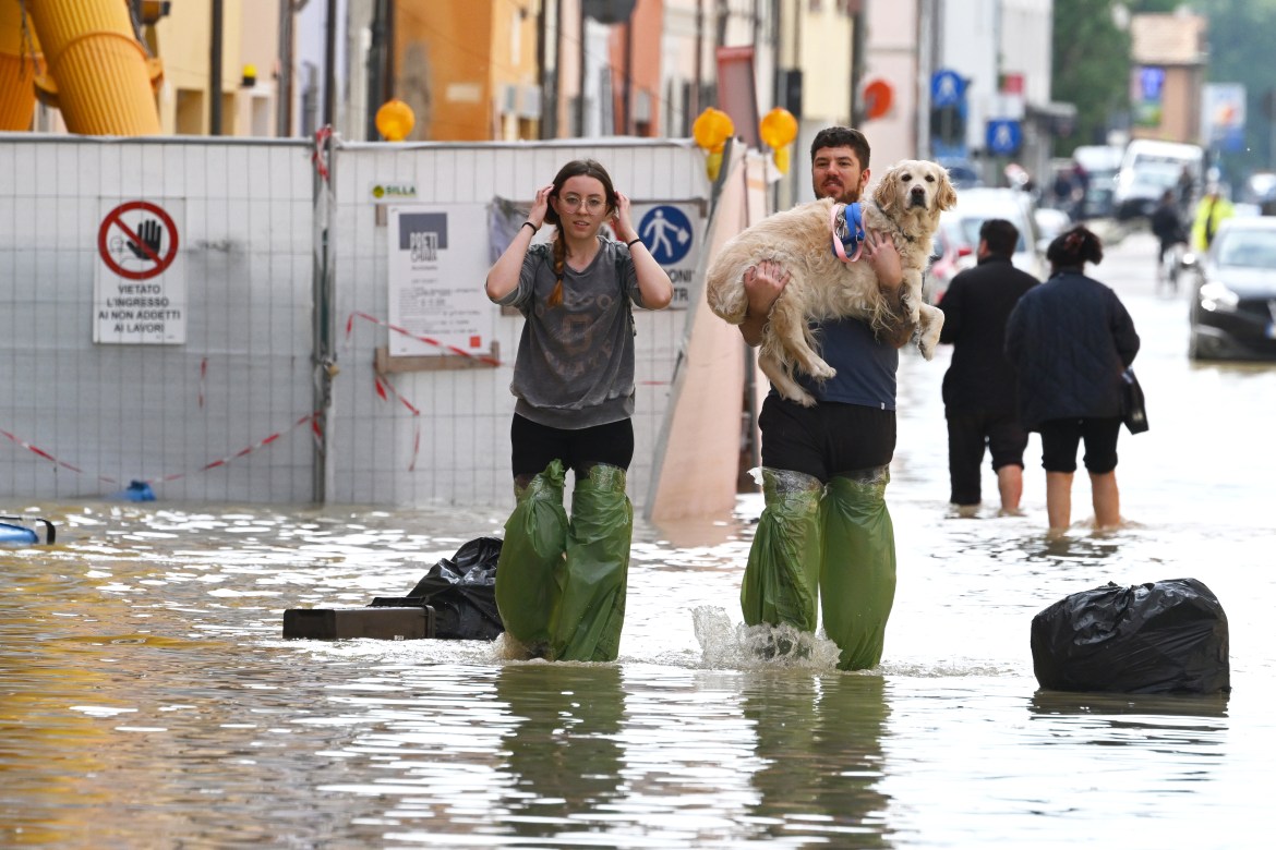 Pedestrians hold their dog in a flooded street in the town of Lugo [Andreas Solaro/AFP]