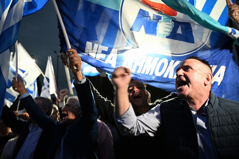 مردم پرچم دموکراسی نوین را پس از اعلام اولین نظرسنجی خارج از مقر حزب راستگرای دموکراسی نوین در مرکز آتن به اهتزاز در می آورند، 21 مه 2023 - حزب محافظه کار نخست وزیر مستعفی یونان تا 11 امتیاز برتری دارد. در نظرسنجی ها، که بعید است منجر به تشکیل دولت شود، نظرسنجی های خروج در 21 مه 2023 نشان داده شد. (عکس: ARIS MESSINIS / AFP)