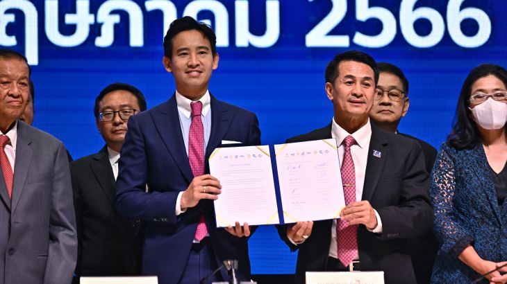 Move Forward Party leader Pita Limjaroenrat and Pheu Thai Party leader Cholanan Srikaew hold a memorandum of understanding signed by eight Thai political parties in agreement to form a new government. They are both dressed in suits and smiling.