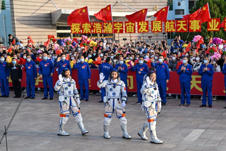 The astronauts waving to the crowd. The crowd has Chinese flags and banners.