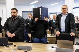 The defendant Lina E, centre, holds a file folder in front of her face at the Dresden Higher Regional Court [Jens Schlueter/AFP]