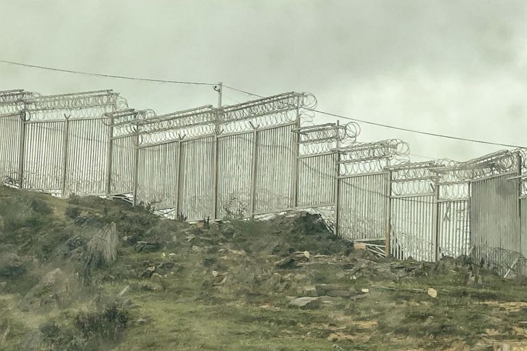 Tall metal fence at China's southern border. It has razor wire and cameras on top. There is greenery around, but no trees.
