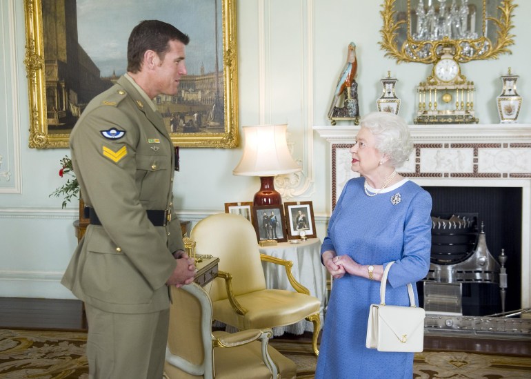 Ben Roberts-Smith meets Britain's Queen Elizabeth shortly after receiving the Victoria Cross. He is in uniform. The queen is wearing a blue dress and carrying a white handbag on her wrist. They look happy and relaxed.