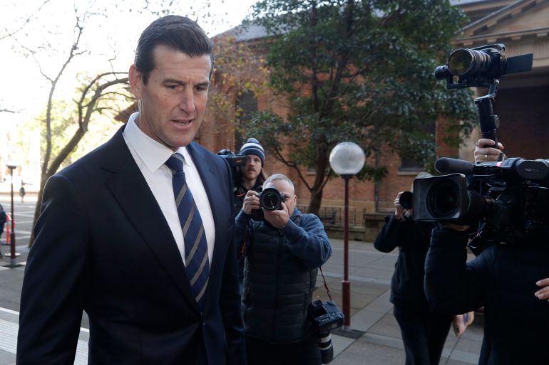 Ben Roberts-Smith arriving in court in 2021. He is in a dark blue suit and tie. He looks imposing. Photographers are taking his picture.