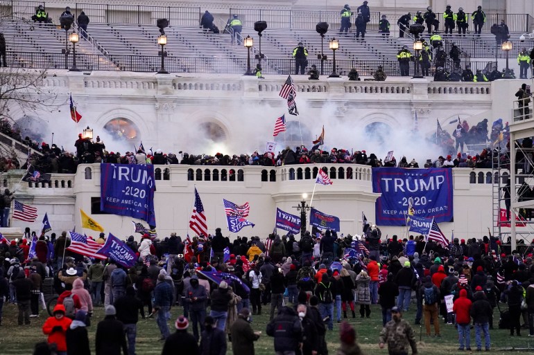 People waving Trump banners and American flags gather before the US Capitol, as smoke and tear gas rise from the riot