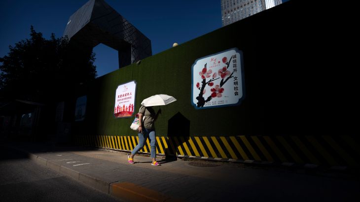 A woman uses an umbrella for shade as she walks through the central business district on an unseasonably warm day in Beijing, Thursday, July 14, 2022.